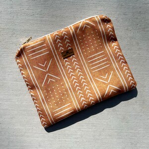 May include: A brown zippered pouch with a white geometric pattern. The pouch has a small brown label with the text "BOHO SMITH" on it.