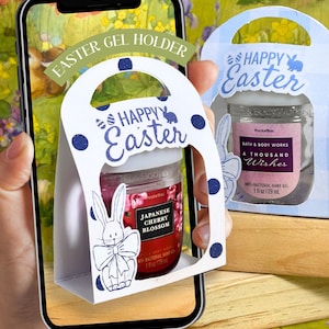 Puede incluir: Un soporte para gel hidroalcohólico con temática de Pascua con un diseño de conejito. El soporte blanco tiene lunares azules y las palabras "Happy Easter". Se ve un frasco de gel hidroalcohólico con "Japanese Cherry Blossom". La imagen se muestra en un smartphone.