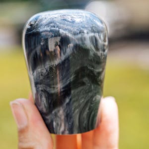 May include: A dark, marbled bottle stopper with swirling patterns of black and white. The stopper has a rounded top and a cylindrical body. The image is a close-up, highlighting the unique texture and design of the decorative piece.