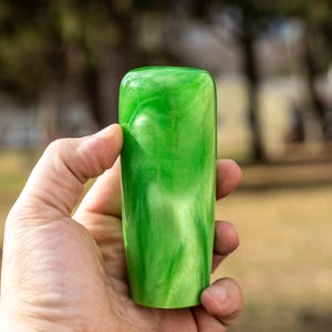 May include: A green, rectangular object with a rounded top and bottom. The object has a marbled appearance with shades of light and dark green. The object is held in a person's hand.