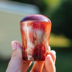 Puede incluir: Un tapón de botella decorativo hecho a mano con un diseño único en espiral. El tapón presenta una mezcla de tonos rojos, blancos y dorados, creando un efecto veteado. La parte superior es redondeada y el cuerpo es ligeramente cónico. El tapón mide aproximadamente 7.6 cm de alto.