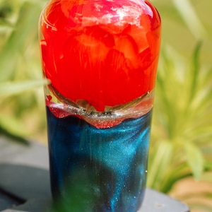 May include: A decorative, cylindrical item with a striking colour scheme. The top is a solid, glossy red, blending into a shimmering blue and teal base. This could be a unique accessory or decorative piece.