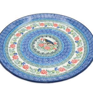 May include: A large, round, blue and white ceramic platter with a floral design and a bird in the center. The platter has a blue rim and a white center with a blue bird perched on a branch with red flowers.
