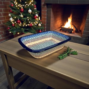 May include: Rectangular ceramic baking dish with a blue rim and intricate patterned design in beige, blue, and brown. The dish sits on a wooden table with a sprig of greenery, a Christmas tree, and a fireplace in the background.