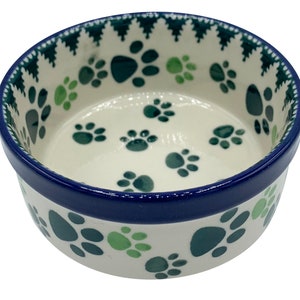 May include: A white ceramic pet bowl with a blue rim and a paw print design in green and blue.