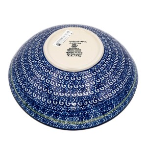 May include: A blue and white ceramic bowl with a decorative pattern. The bowl is hand-made in Poland and has the text "UNIKAT-AMT J.CHYEA CERAMIKA ARTYSTYCZNA BOLESLAWIEC HAND MADE IN POLAND K.K.-776" on the bottom.