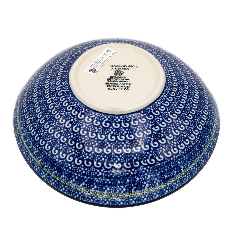 May include: A blue and white ceramic bowl with a decorative pattern. The bowl is hand-made in Poland and has the text "UNIKAT-AMT J.CHYEA CERAMIKA ARTYSTYCZNA BOLESLAWIEC HAND MADE IN POLAND K.K.-776" on the bottom.
