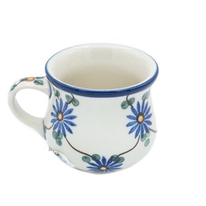 May include: A white ceramic mug with a blue rim and floral design. The flowers are blue with yellow centers and green leaves.