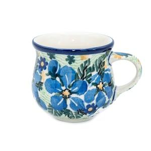 May include: A white ceramic mug with a blue and green floral pattern. The mug has a rounded body and a handle.