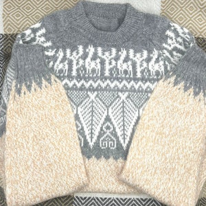 May include: A gray and beige knitted sweater with a white geometric pattern. The sweater has a crew neck and long sleeves.