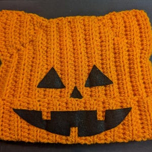 Flat lay of the orange ribbed crochet cat beanie featuring black felt jack-o-lantern eyes, nose, and mouth.