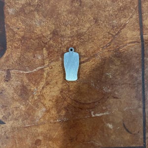 May include: A small, silver-colored charm in the shape of a beer glass. The charm has a small hole at the top for attaching to a necklace or bracelet. The charm is made of a shiny metal and has a smooth surface.