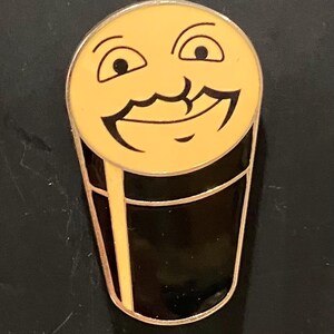 Puede incluir: Un pin de esmalte negro y amarillo de un vaso de cerveza sonriente con bigote.