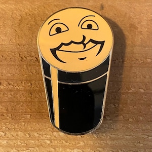 May include: A gold-colored pin shaped like a glass of beer with a smiling face on the top. The beer glass is black with a gold rim.
