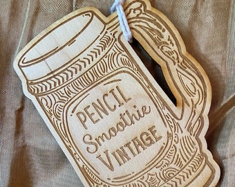 May include: A wooden cutout of a vintage-style glass with the text "Pencil Smoothie Vintage" engraved on it.