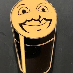 Puede incluir: Un pin de esmalte amarillo con forma de vaso de cerveza con una cara sonriente y un bigote.