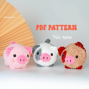 May include: Three crocheted pig plushies in different colors: pink, white with gray spots, and brown with red spots. The plushies have pink snouts and black eyes. The text "PDF PATTERN No sew" is above the plushies.