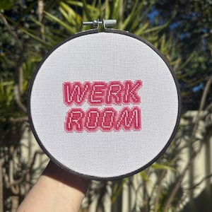 May include: A white embroidery hoop with a pink cross-stitch design that reads "Werk Room".