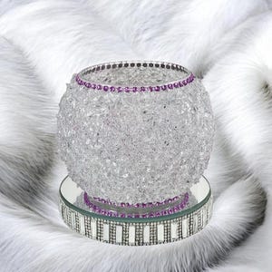 May include: A purple crushed glass vase with a purple rhinestone trim. The holder is sitting on a mirrored base with a silver rhinestone trim.