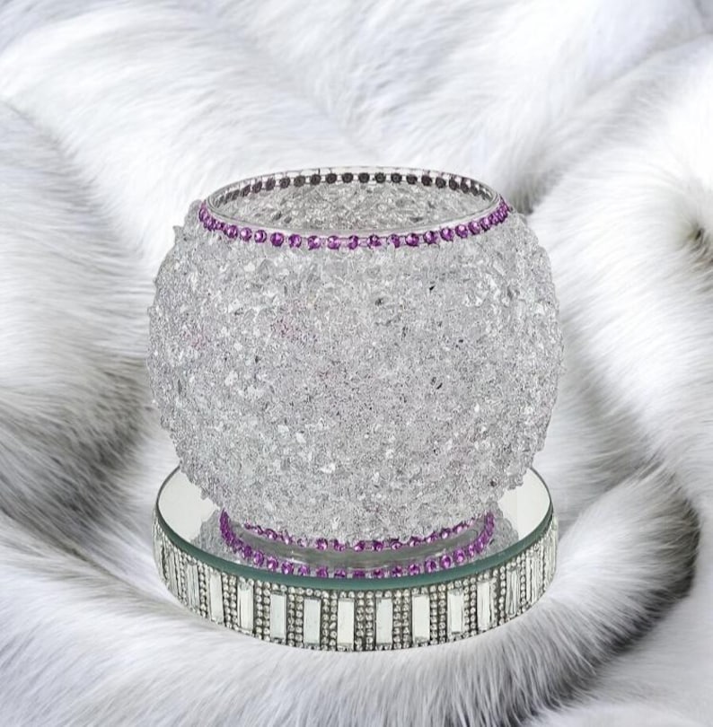 May include: A purple crushed glass vase with a purple rhinestone trim. The holder is sitting on a mirrored base with a silver rhinestone trim.