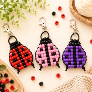 May include: Three ladybug-shaped keychains crafted from plastic beads on black cord, each featuring a silver-tone metal lobster clasp. The ladybugs are colored red, light pink, and purple, all with black bead accents and a central black stripe.