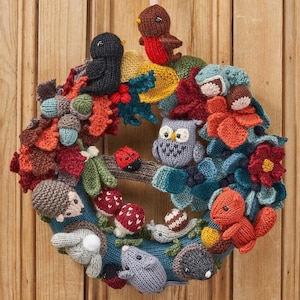 Puede incluir: Una corona tejida a mano con criaturas del bosque y follaje otoñal. La corona incluye una variedad de animales como pájaros, un búho, un erizo, una ardilla y un ratón, junto con setas, bellotas y hojas. La paleta de colores incluye tonos de azul, naranja, rojo y marrón.