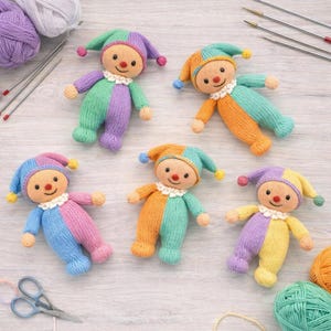 May include: A collection of six knitted jester dolls in various color combinations, including green and purple, orange and teal, and blue and pink. Each doll has a smiling face, a ruffled collar, and a matching hat with a pom-pom.