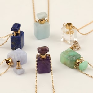 Pode incluir: Seis colares com frasco de perfume de cristal. Cada frasco é de uma cor e forma diferentes, incluindo transparente, azul, verde, roxo e branco. Os frascos estão todos presos a correntes douradas.