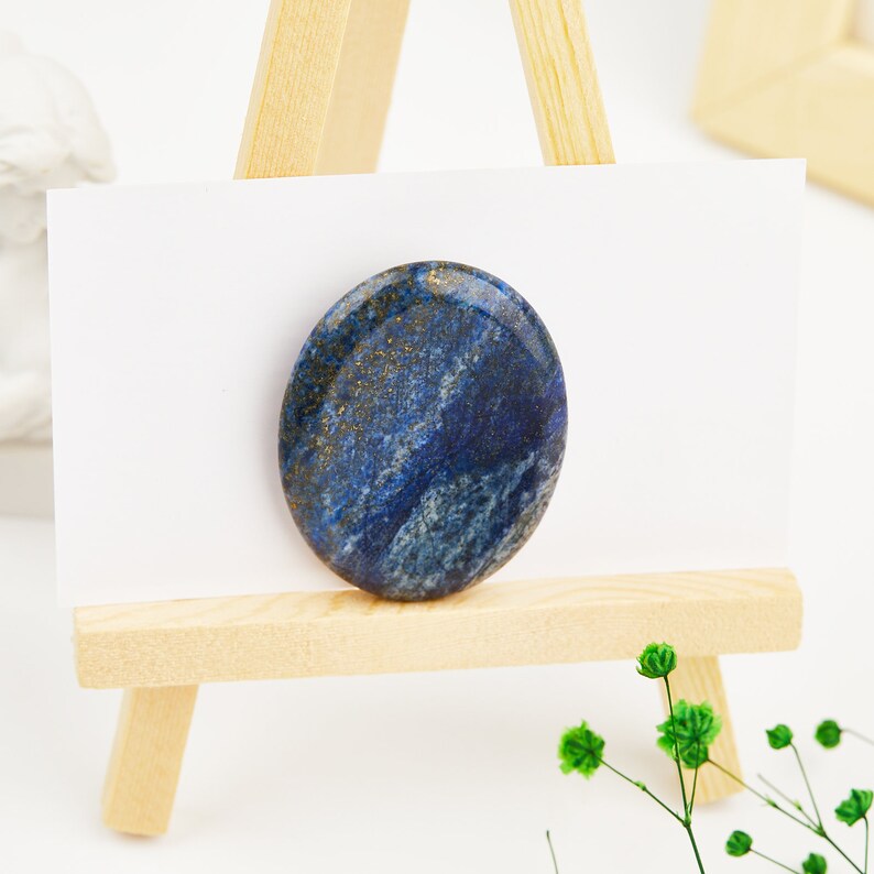 May include: A smooth, oval-shaped lapis lazuli stone with gold flecks and blue and white swirls. The stone is displayed on a small wooden easel.