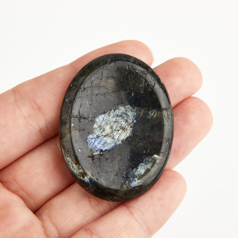 May include: A black oval-shaped labradorite palm stone with iridescent blue and white flashes.