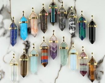 May include: A collection of 18 gold-capped crystal point pendants with various colors and patterns. The pendants are arranged in a semi-circle on a white marble surface.