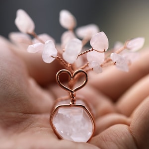 Könnte beinhalten: Ein rosafarbener Kristall-Herzbaum mit einer Kupferdrahtbasis und einem herzförmigen Drahtdesign. Der Baum besteht aus kleinen rosa Kristallen und liegt in der Hand einer Person.