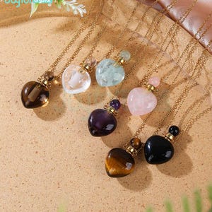 Op de afbeelding: Zeven gouden hartvormige kettingen met verschillende gekleurde kristallen hangers. De hangers zijn van amethist, rozenkwarts, tijgeroog, zwarte onyx, helder kwarts, aquamarijn en bruin.