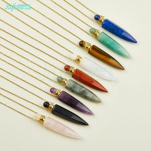 Pode incluir: Dez colares de corrente de ouro com pingentes de ponta de cristal. Cada pingente é de uma cor diferente e tem um pequeno tampão de garrafa de ouro. As cores dos pingentes são: lápis-lazúli, aventurina verde, olho de tigre, branco, jaspe vermelho, labradorita, ametista, obsidiana negra e quartzo rosa.