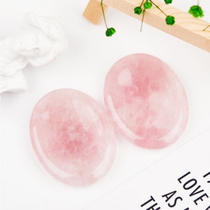 May include: Two smooth, oval-shaped rose quartz stones. The stones are a light pink color and have a polished finish.