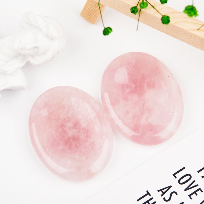 May include: Two smooth, oval-shaped rose quartz stones. The stones are a light pink color and have a polished finish.