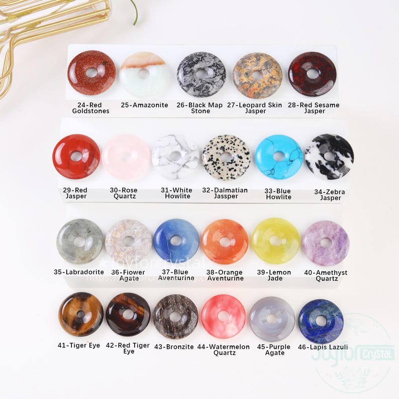 Puede incluir: Una colecci&oacute;n de colgantes de piedras preciosas en forma de rosquilla en varios colores y patrones. Los colgantes incluyen Red Goldstones, Amazonita, Black Map Stone, Leopard Skin Jasper, Red Sesame Jasper, Red Jasper, Rose Quartz, White Howlite, Dalmatian Jasper, Blue Howlite, Zebra Jasper, Labradorita, Flower Agate, Blue Aventurine, Orange Aventurine, Lemon Jade, Amethyst Quartz, Tiger Eye, Red Tiger Eye, Bronzita, Watermelon Quartz, Purple Agate y Lapis Lazuli.