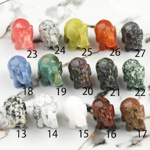 May include: Twenty-seven small elephant figurines carved from different types of stone. The elephants are in various colors, including green, blue, red, white, brown, and black.
