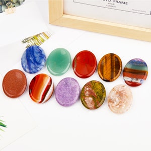 May include: Ten smooth, oval-shaped polished stones in various colors, including red, green, blue, purple, brown, and white. The stones are arranged in a row on a white surface.