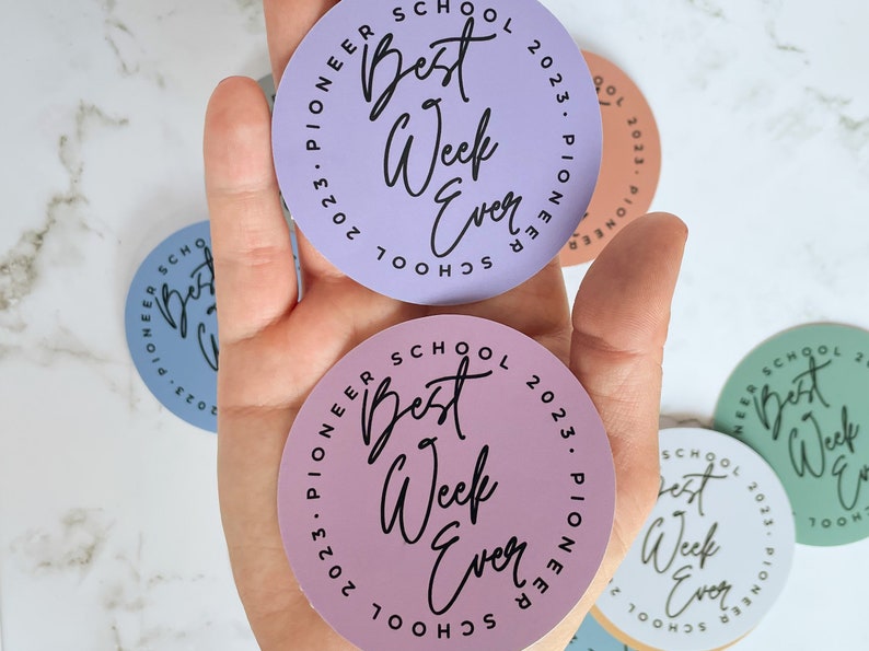 K&ouml;nnte beinhalten: Drei runde Aufkleber mit dem Text "Best Week Ever" in einem Kreis mit den Worten "Pioneer School 2023" au&szlig;en herum. Die Aufkleber sind in Lila, Rosa und Gr&uuml;n.