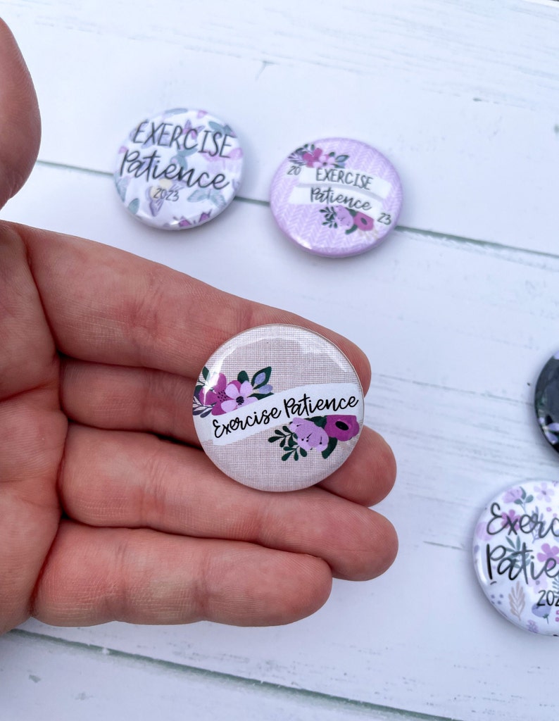 May include: Three round buttons with a floral design and the text "Exercise Patience" in white. The buttons are on a white wooden surface.
