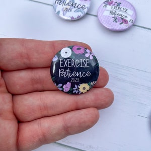 May include: A black button with a floral design and the text "EXERCISE PATIENCE 2023".