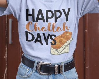 Könnte beinhalten: Ein hellblaues T-Shirt mit dem Text "Happy Challah Days" in schwarzen Buchstaben und einer Grafik eines Challah-Brot. Das Model trägt eine schwarze Mütze und Jeans-Shorts.