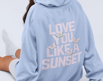 May include: A light blue hooded sweatshirt with the text "LOVE YOU LIKE A SUNSET" printed on the back. The text is in pink with small butterfly graphics.