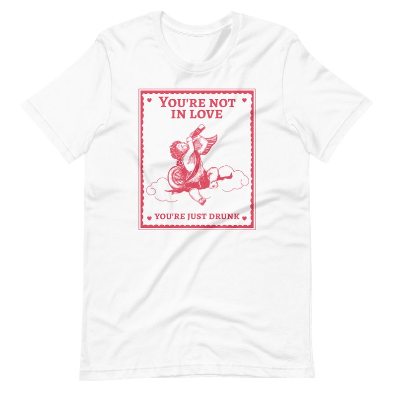 Pu&ograve; includere: Maglietta bianca con una grafica rossa di un cupido che beve da una bottiglia con il testo "You're not in love. You're just drunk."