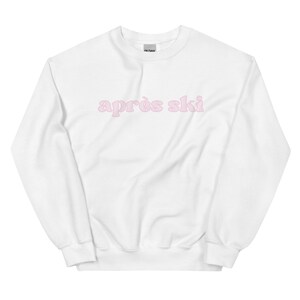 Op de afbeelding: Witte trui met de tekst "apr&egrave;s ski" in roze letters.