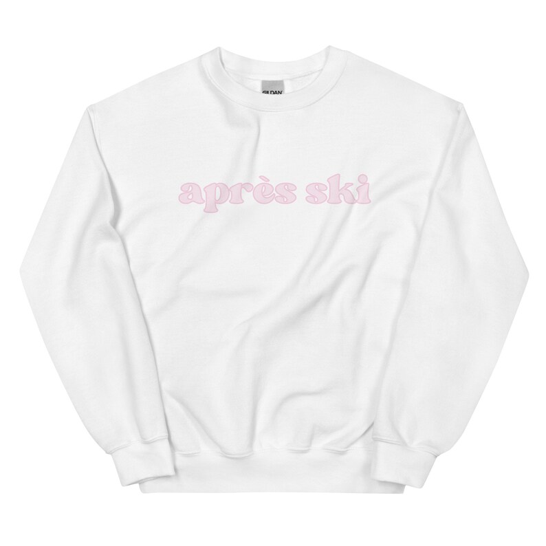 Op de afbeelding: Witte trui met de tekst "apr&egrave;s ski" in roze letters.