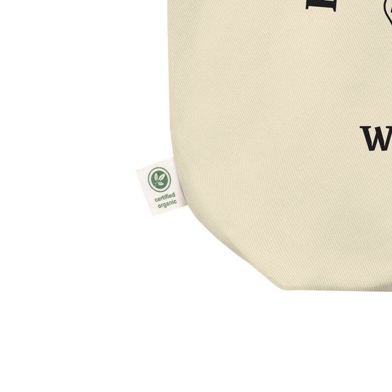 May include: A close-up of a beige tote bag with a black text graphic and a green "certified organic" label.