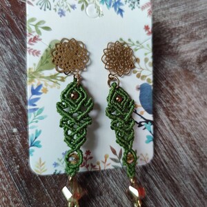 Peut inclure: Une paire de boucles d'oreilles vertes et dor&eacute;es avec un design d&eacute;licat et complexe. Les boucles d'oreilles pr&eacute;sentent un petit charme rond de couleur dor&eacute;e en haut, suivi d'une section nou&eacute;e verte et d'une perle de cristal en bas.