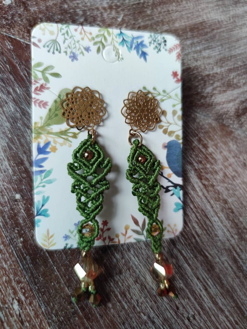 Peut inclure: Une paire de boucles d'oreilles vertes et dor&eacute;es avec un design d&eacute;licat et complexe. Les boucles d'oreilles pr&eacute;sentent un petit charme rond de couleur dor&eacute;e en haut, suivi d'une section nou&eacute;e verte et d'une perle de cristal en bas.